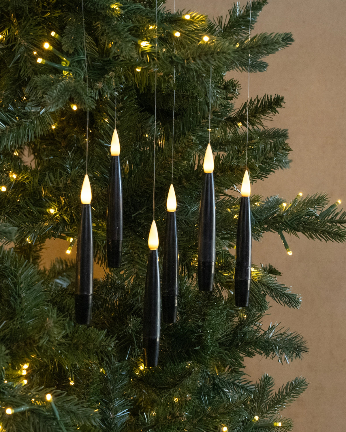 Black LED hanging candles by Faire decorate a green Christmas tree with warm yellow lights, festive and cozy.