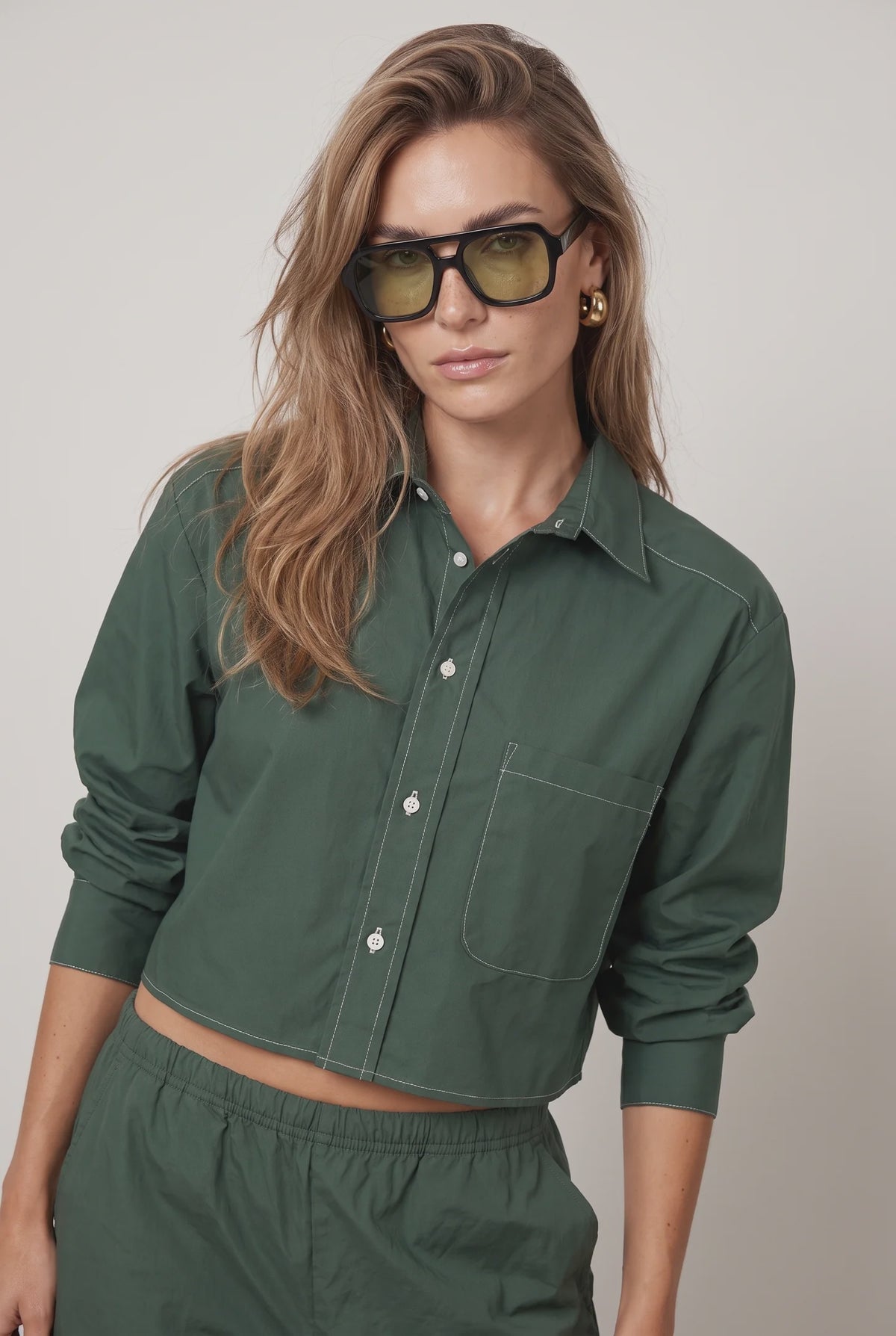 Olive-green sunglasses paired with THE SHIRT’s white-stitched Harper shirt and matching pants, modern casual style.