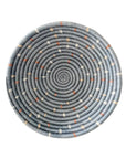 The Kitopo Small Bowl by Faire is a round, handmade basket tray woven from sisal with gray-blue concentric rings and white and brown stitch accents, shown against a white background.