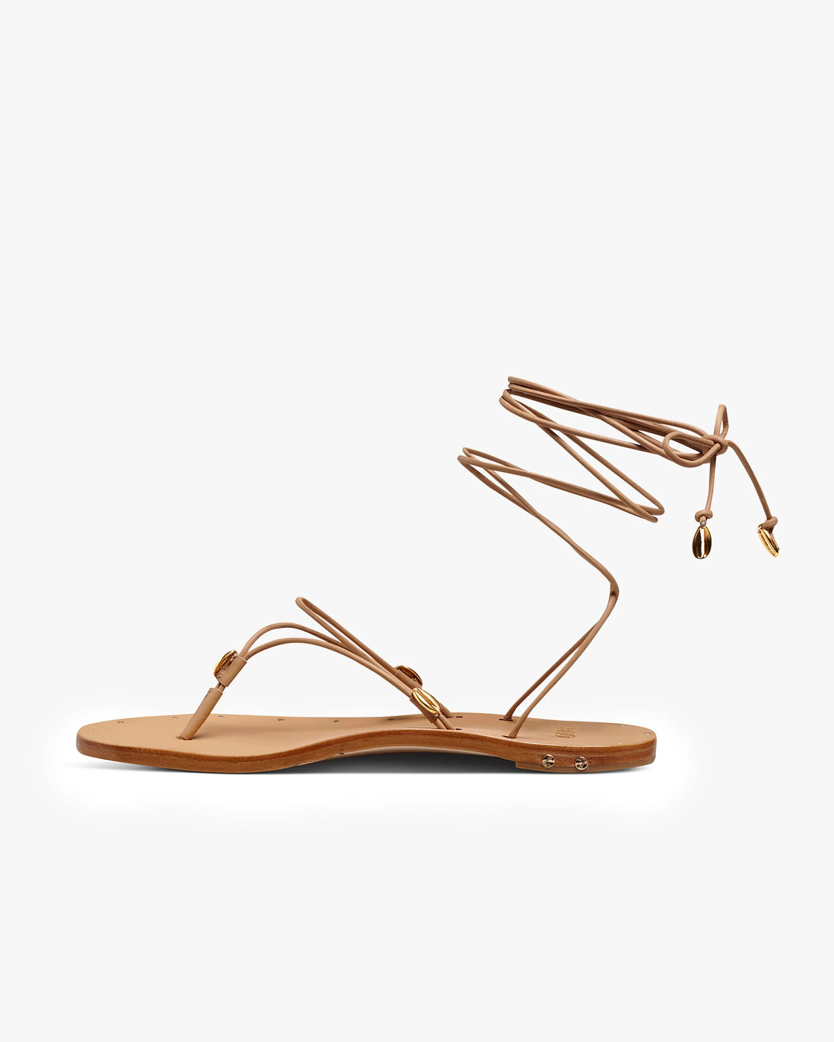 The Beek Koha Sandal is a tan leather sandal with thin straps and an adjustable ankle-tie, accented by small gold shell details at the tie ends. Shown in side view on a white background.