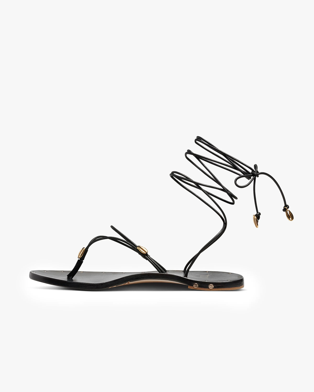 The Beek Koha Sandal is a black leather minimalist sandal with a toe strap, thin adjustable ankle lace with gold shell accents, and molded arch support for all-day comfort.