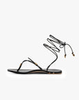 The Beek Koha Sandal is a black leather minimalist sandal with a toe strap, thin adjustable ankle lace with gold shell accents, and molded arch support for all-day comfort.