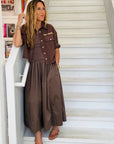 A woman stands on white stairs wearing the KR Tank Dress by Kerri Rosenthal with a matching short-sleeved jacket. She has long hair, sandals, bracelets, and colorful books and art appear in the background.