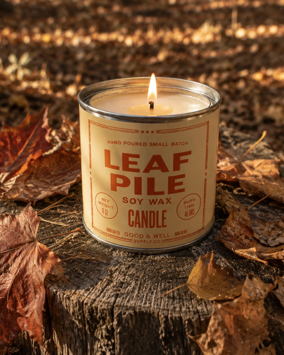 Faire Leaf Pile Soy Candle lit on a tree stump, autumn leaves and warm sunlight evoke cozy fall style.
