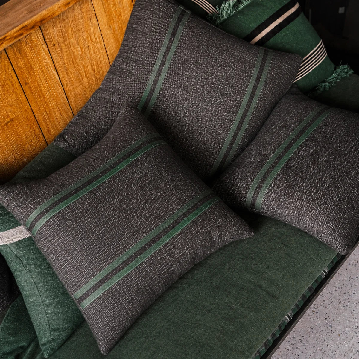 Leo Linen Pillows with green stripes by Libeco Home displayed on a green bench against a wooden wall.