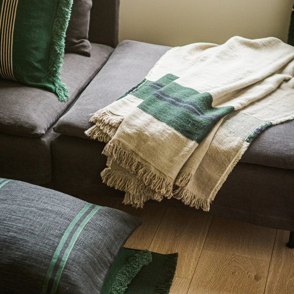Libeco Home Omaha Stripe beige and green coverlet styled on a dark gray sofa with green-accented pillows.