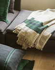 Libeco Home Omaha Stripe beige and green coverlet styled on a dark gray sofa with green-accented pillows.