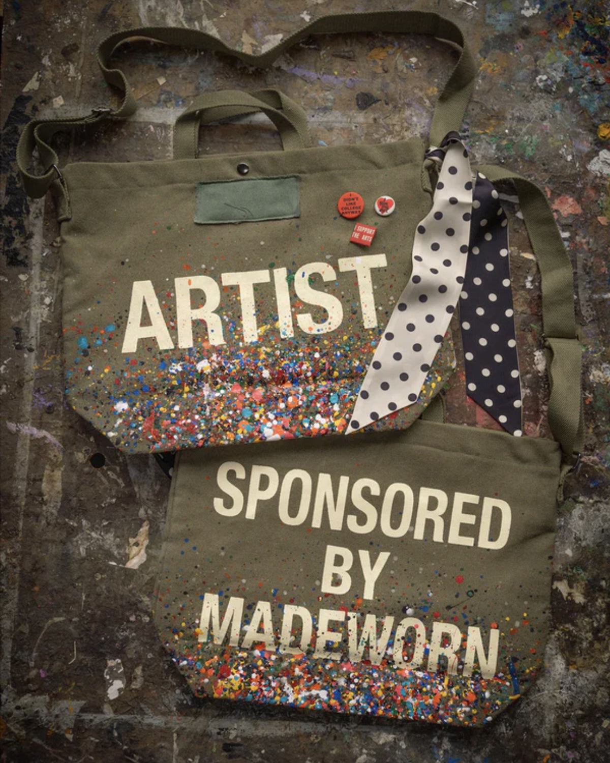 The limited-edition Artist Tote by Made Worn is crafted from cotton canvas with paint splatters, polka dot ribbons, confetti accents, and playful pins—one says "ARTIST," the other "SPONSORED BY MADEWORN." Each bag is truly unique.
