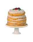 The Maileg Party cake and cake stand, Mouse - Off White, features layers of cake with cream filling and colorful fruit accents. This delightful piece is an ideal party decoration, standing out beautifully against a white background.