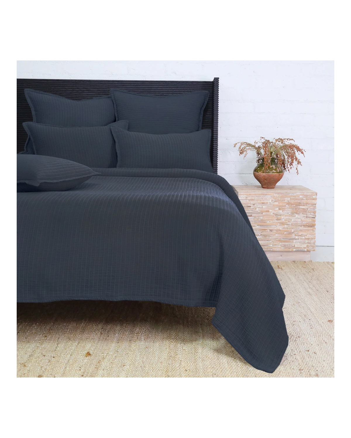 Dark gray ribbed cotton bedding set by Pom Pom, shown with pillows and bedside plant in a modern bedroom.
