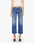 A person wearing Mother’s The Mid Rise Maven Flood jeans in blue, a white sleeveless top, black pointed-toe heels, and a gold bracelet stands against a plain white background.