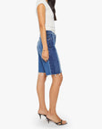 Woman in a white t-shirt, Mother’s Mid Rise Maven Bermuda Fray shorts, and black heeled sandals stands in profile against a plain white background.
