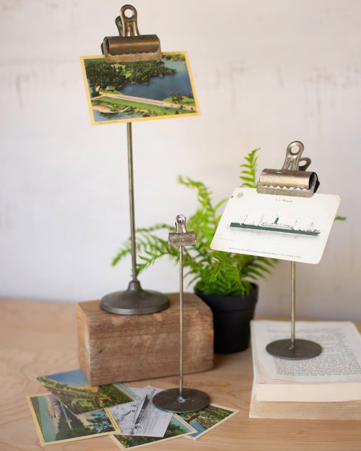 Metal note clips by Kalalou hold postcards on a desk, styled with books, wood accents, and a potted fern for Bungalow.