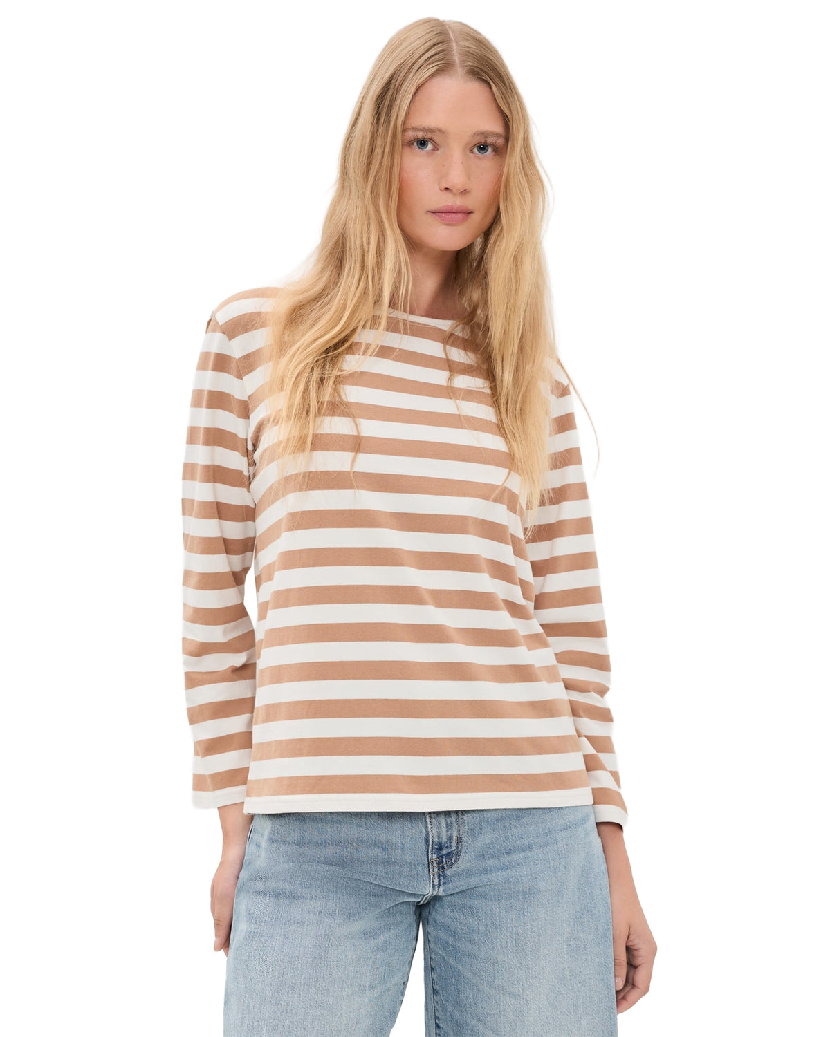 A woman with long blonde hair wears the MILLS POND STRIPED T by Denimist— a beige and white striped lightweight jersey tee—paired with light blue jeans, standing against a plain white background.