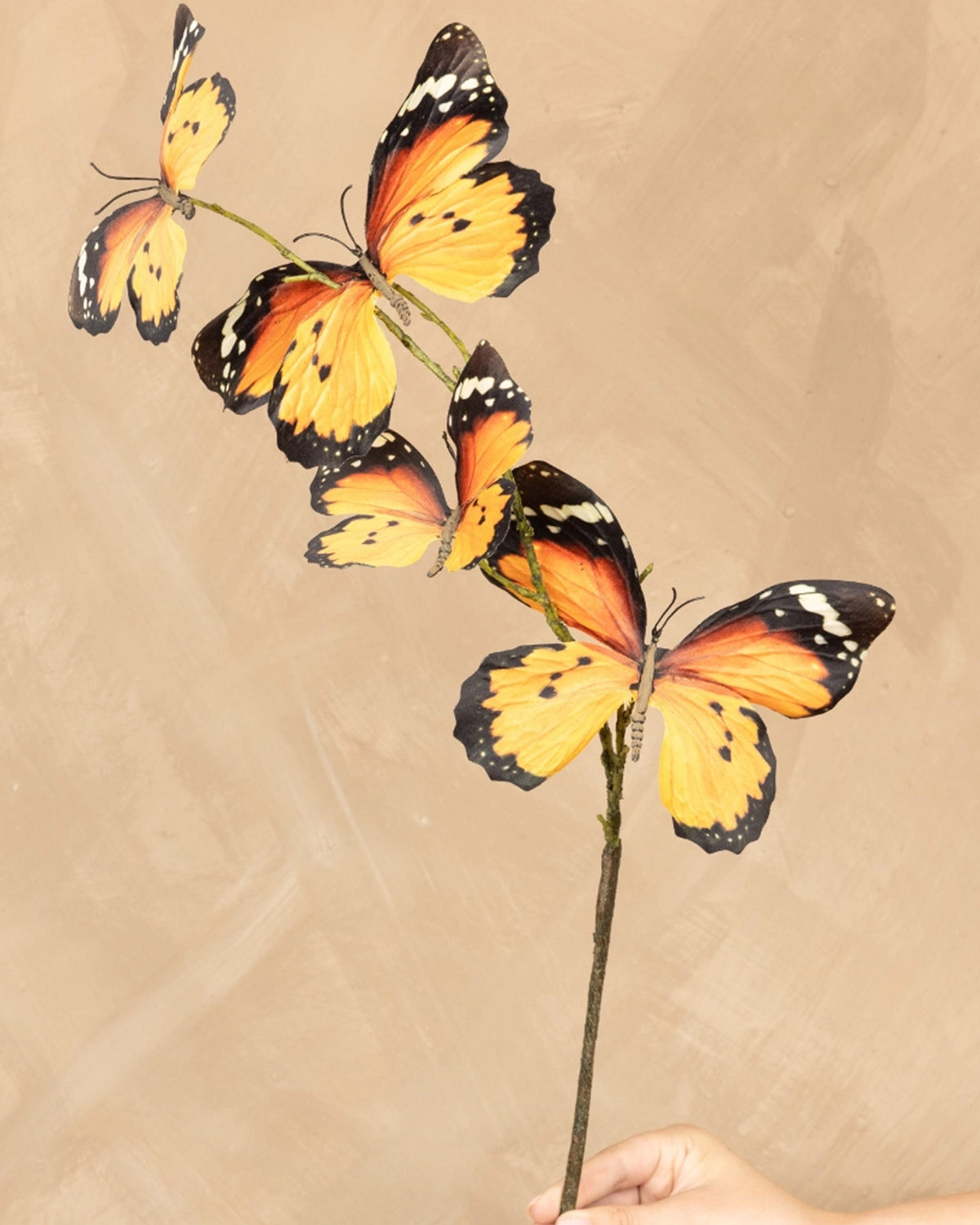 Faire Orange Monarch Butterfly Stem with three butterflies, held in hand, perfect for spring decor at Bungalow Furniture.