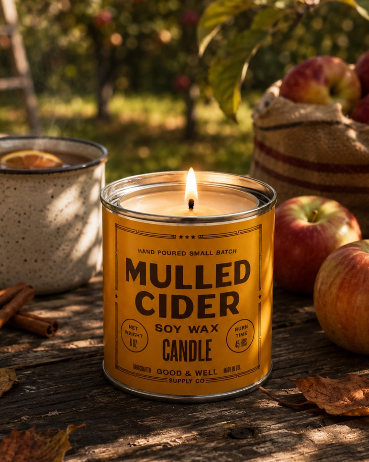 Faire Mulled Cider Soy Candle lit on a table, styled with apples and cinnamon for a cozy autumn setting at Bungalow.