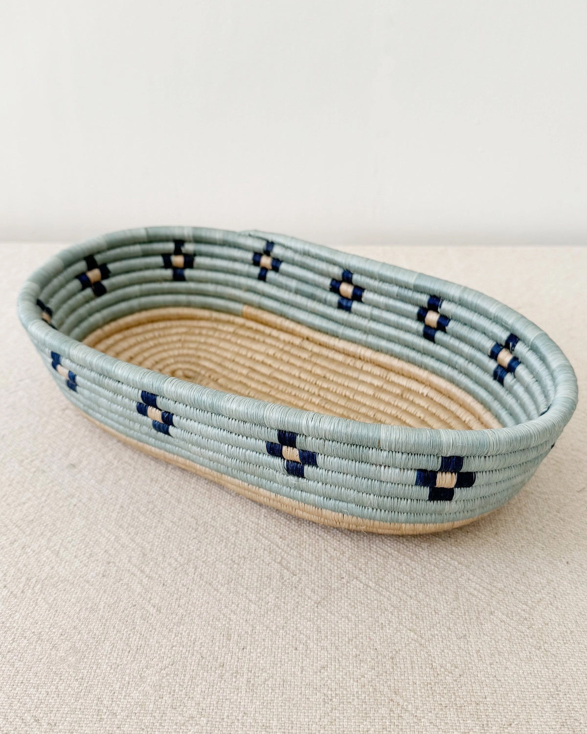Handcrafted blue and beige woven Ngozi Bread Basket by Faire on a beige surface, artisan-made in Rwanda.