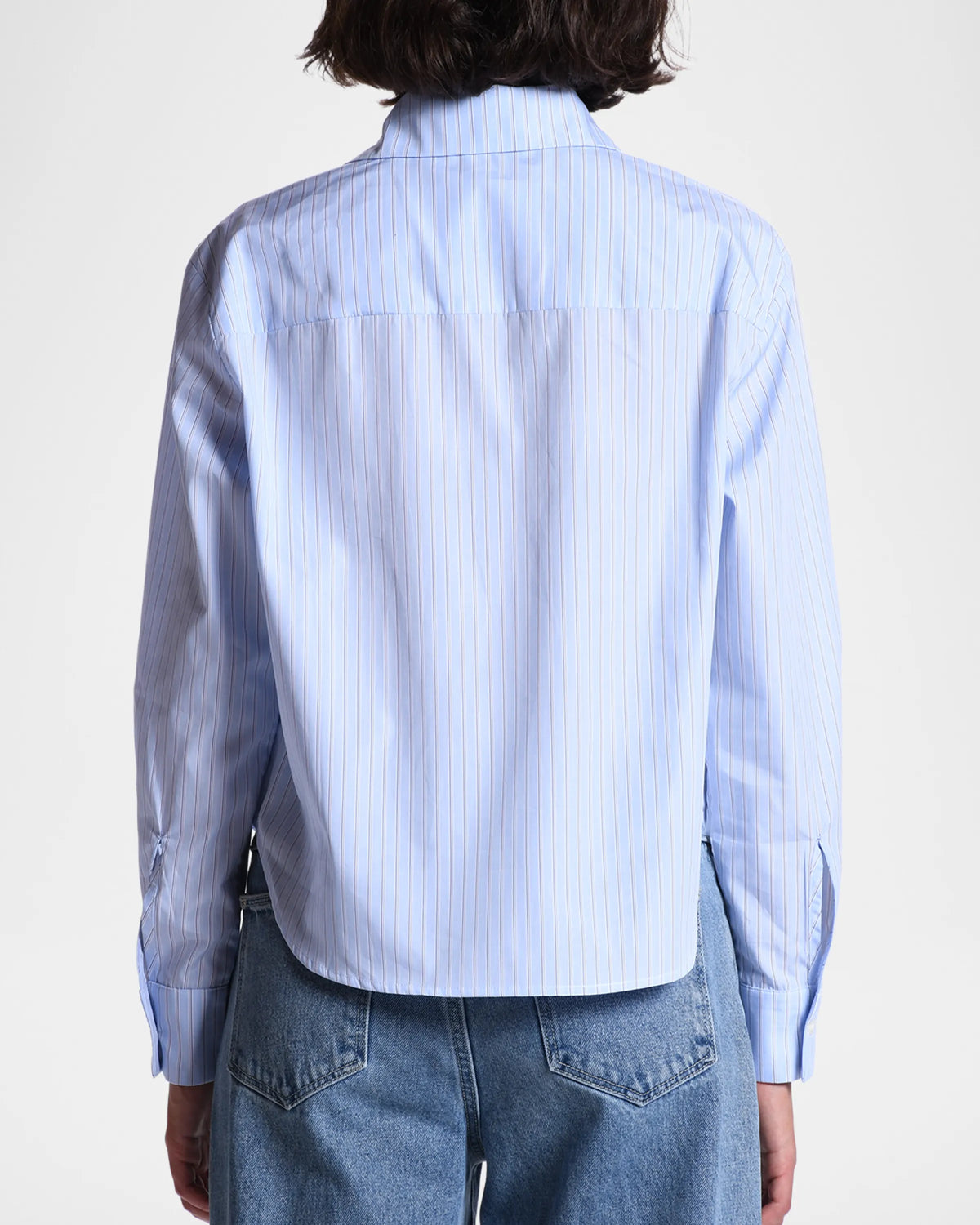 A person is seen from the back wearing The Belle by Cissa—a light blue, relaxed-fit Egyptian cotton shirt with thin vertical stripes—paired with blue jeans, set against a plain white background.