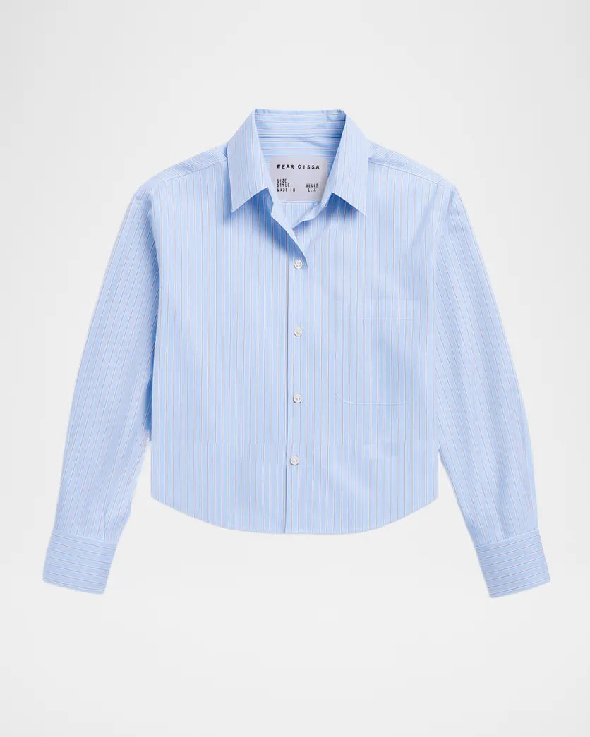 The Belle by Cissa: a light blue, long-sleeve shirt featuring white vertical stripes, relaxed fit, pointed collar, and single chest pocket, shown on a plain white background.