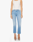 A person wears Mother’s The Outsider Flood Fray light blue straight-leg jeans with frayed hems, a sleeveless white top, and pointed-toe clear heels, standing against a white background.