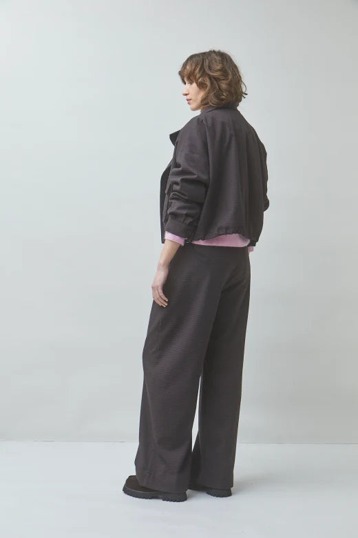 SUNCOO coffee brown pants and oversized jacket styled with pink top in a minimalist studio, model turned away.