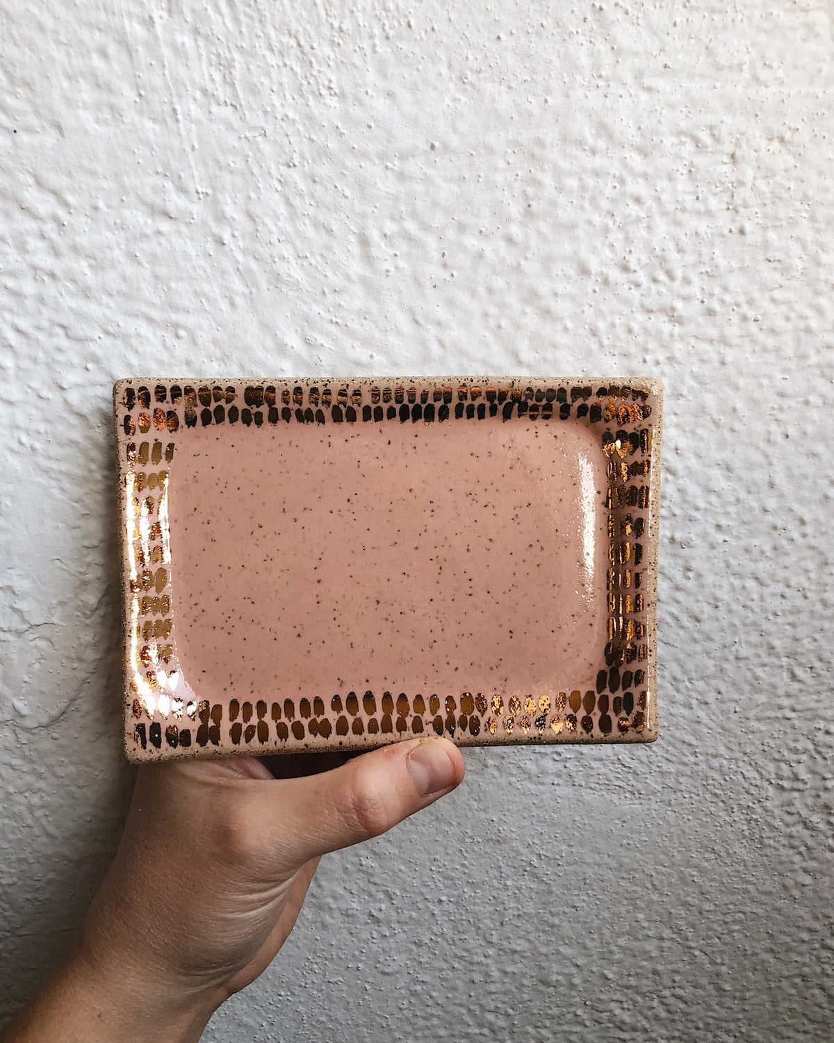 Faire Peach and Gold Mini Vanity Tray in glossy, speckled ceramic, displayed by a textured wall.
