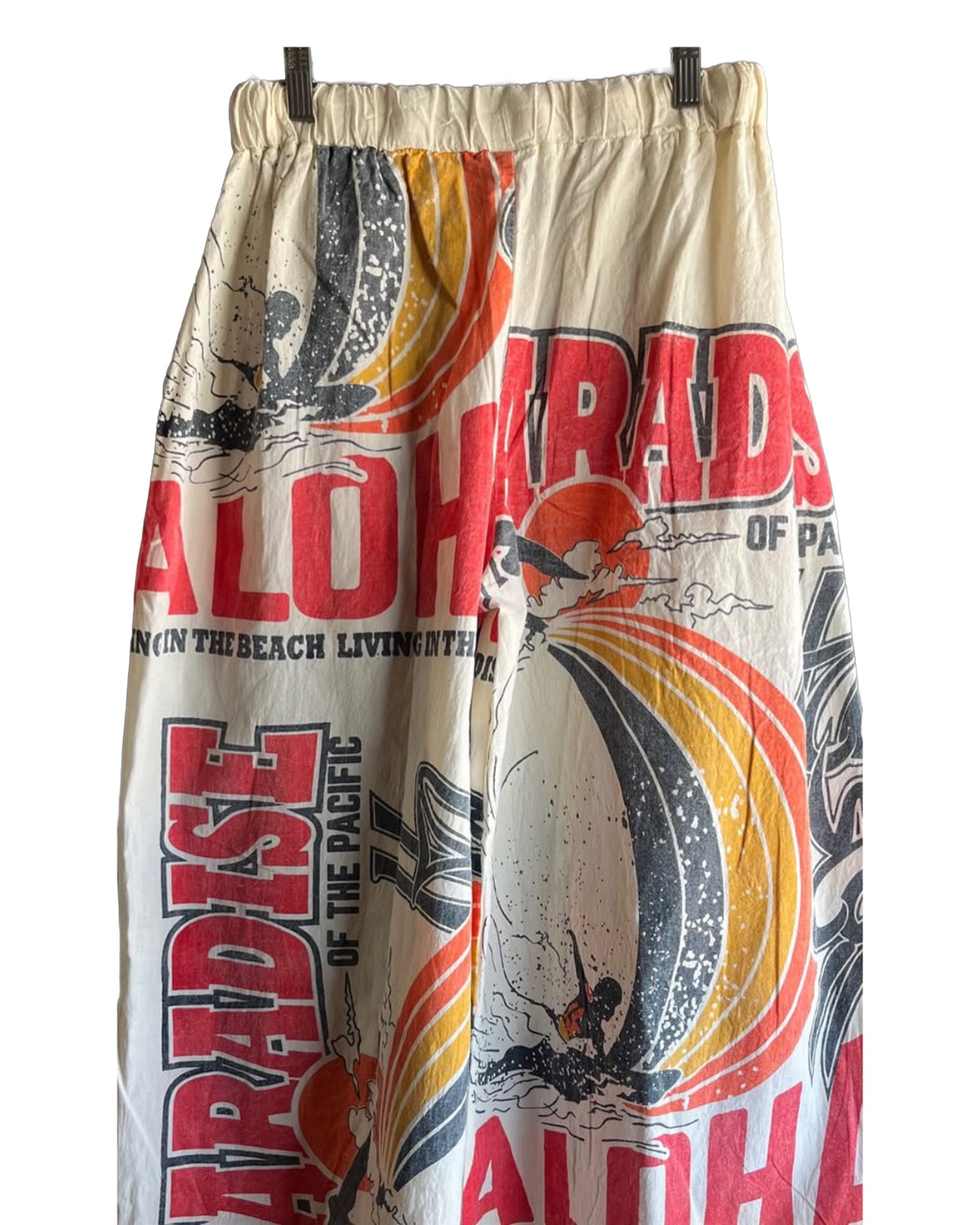 Ping Pong Surf Club’s Aloha Paradise Jogers feature vibrant red and orange "ALOHA" and "PARADISE" prints, surfers, waves, and palm trees—bringing bold Hawaii vibes and island comfort to your summer style.