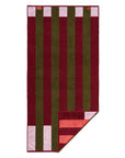 The Typical Pink/Burgundy Stripe Bath Towel is rectangular, reversible, and features bold vertical stripes in burgundy and olive green, plus a small pink and red striped section at one corner.