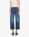 A person wearing a white short-sleeve top, Mother’s The Half-Pipe Ankle high-waisted jean in SUPERIOR denim, and dark blue sandals stands against a plain white background.