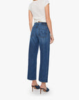 A woman stands with her back turned, wearing a white short-sleeve top, blue heeled mules, and Mother’s The Half-Pipe Ankle high-waisted jeans in a dark blue wash with wide legs.