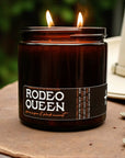 Brown jar Rodeo Queen Candle with twin flames by Faire, soy coconut wax, glowing outdoors on a round surface.