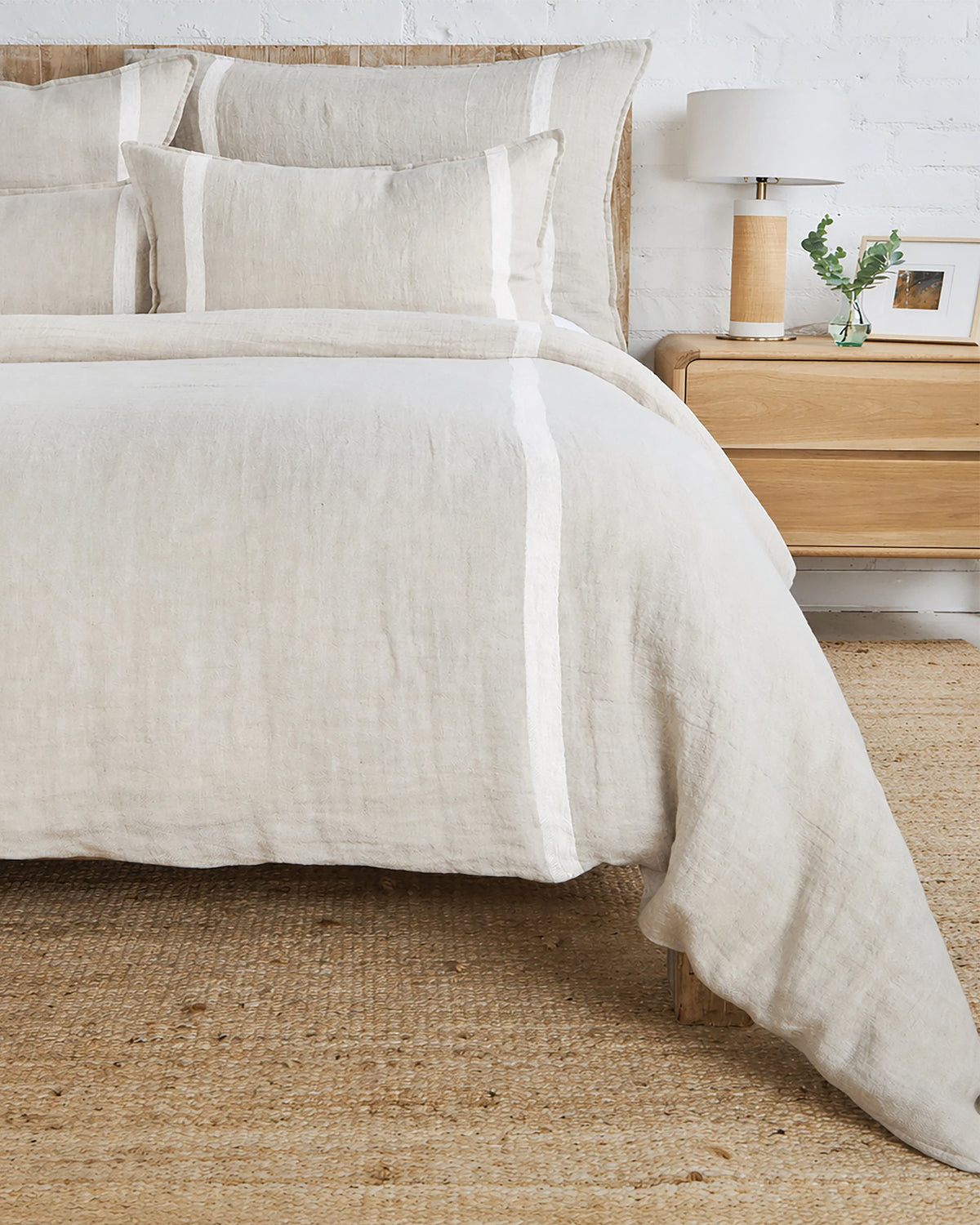 Beige linen Rory King duvet with white stripes by POM POM, styled beside a wooden nightstand in a cozy bedroom.