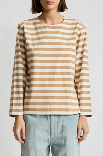 A person in a beige and white Denimist MILLS POND STRIPED T and light blue jeans stands against a plain white background. The long-sleeved tee, evoking casual style, adds a timeless touch. The person's head is partially out of frame.