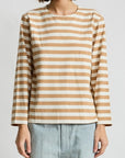 A person in a beige and white Denimist MILLS POND STRIPED T and light blue jeans stands against a plain white background. The long-sleeved tee, evoking casual style, adds a timeless touch. The person's head is partially out of frame.