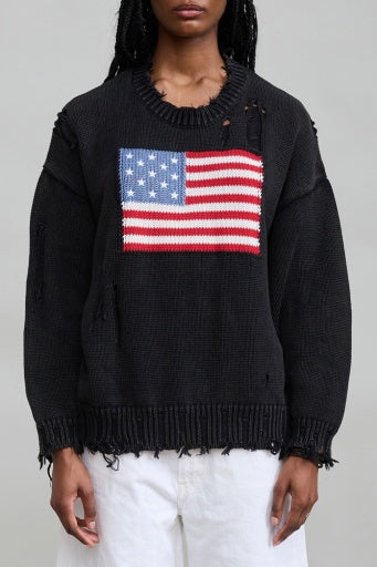 Distressed black Denimist American Flag Sweater with white pants, minimal backdrop, casual modern style.