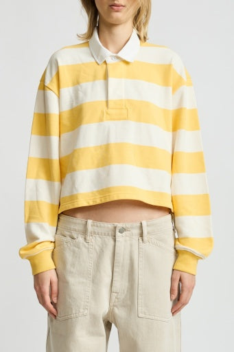 A person wearing the Denimist CHARLIE RUGBY, a yellow and white boxy fit cropped rugby top with a white collar, paired with loose beige pants, stands against a plain background.