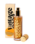 A gold bottle of Faire Shimmer Body Oil with a pump top stands before its branded box, featuring bold black and gold text that highlights its luxurious formula to enhance your skin's moisture barrier and radiant glow.