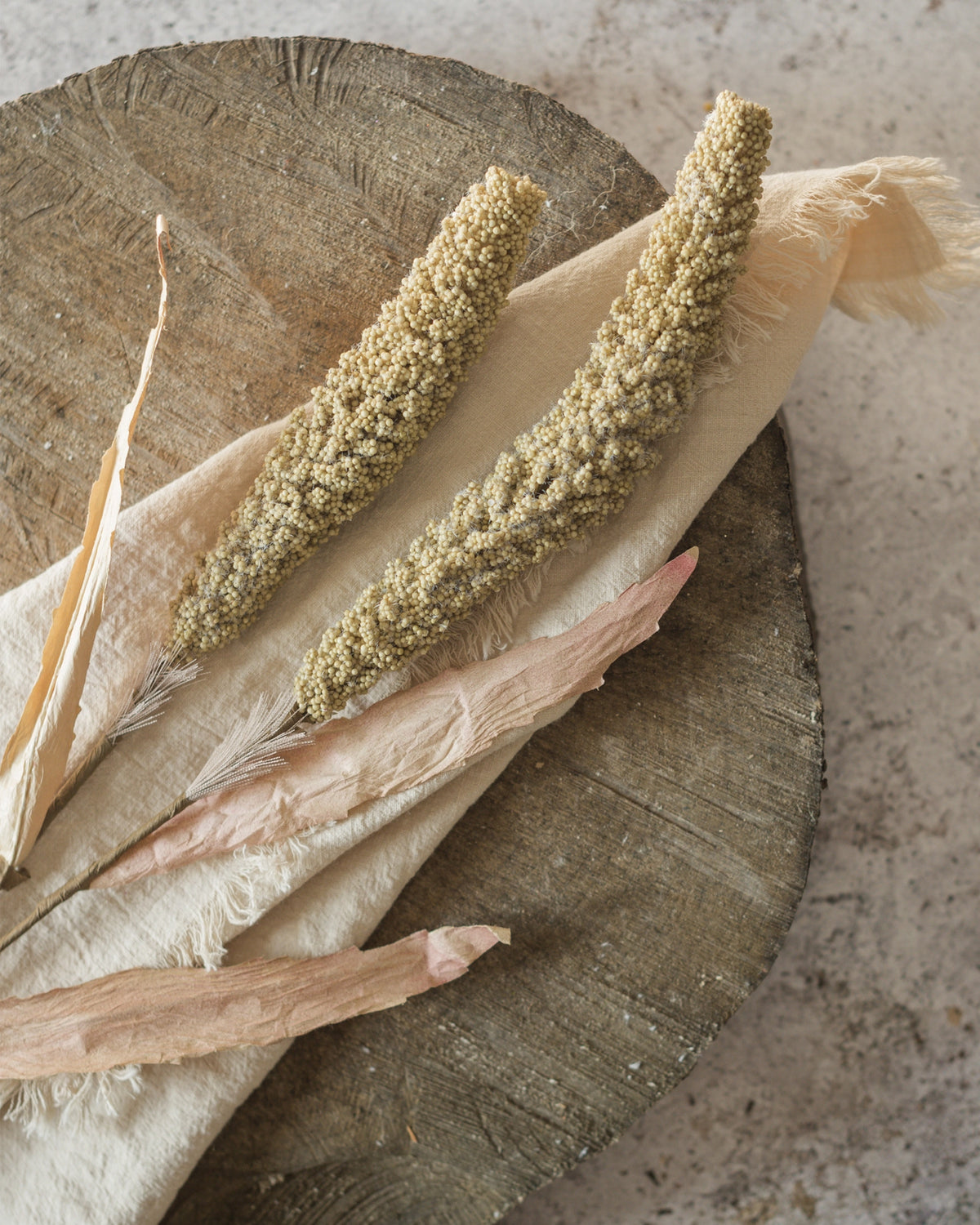 Tan sorghum spray by Faire styled on beige fabric, creating a subtle natural accent for home decor.
