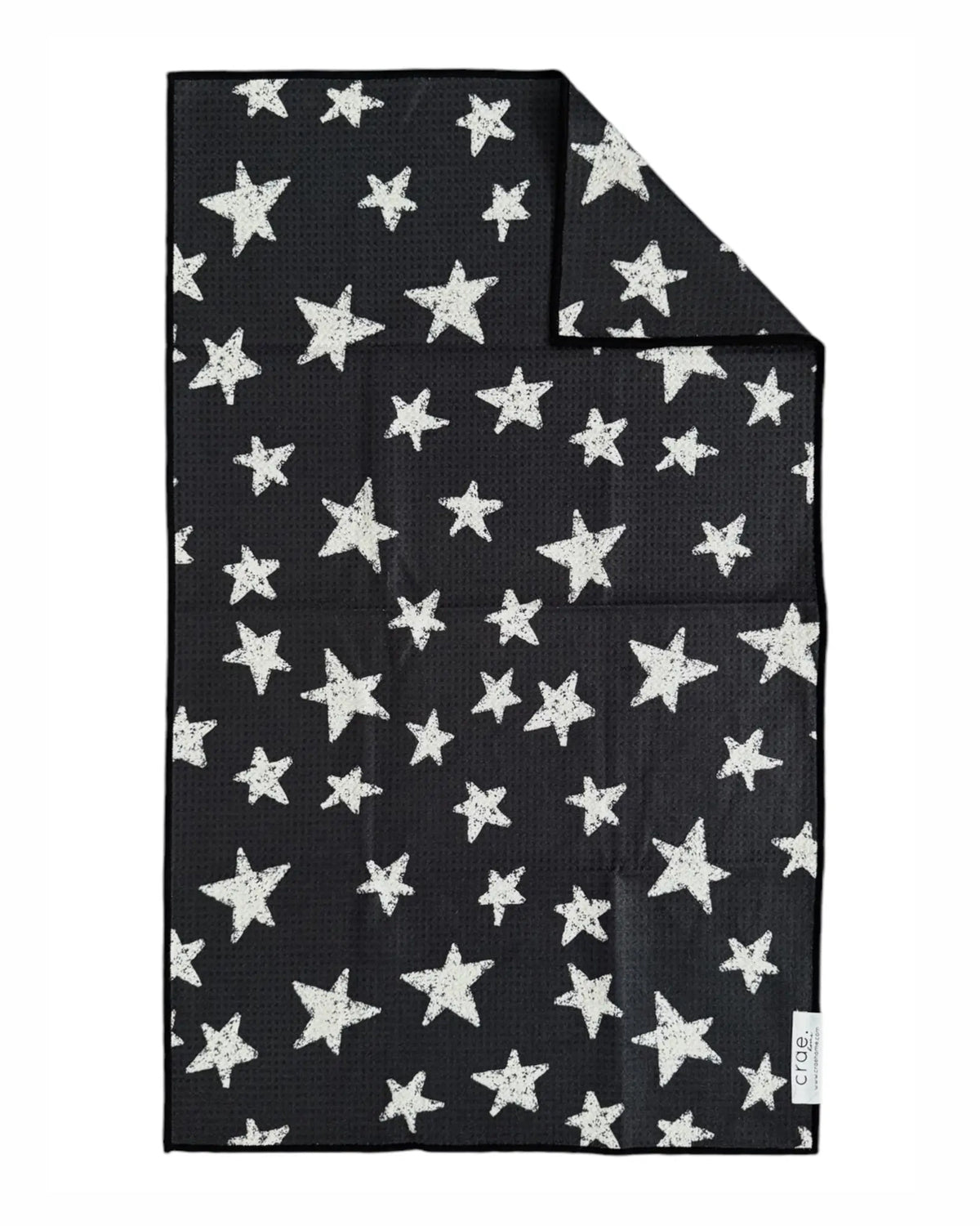 The Faire "Hand Towel : Into The Stars" is a black waffle weave microfiber towel with white stars in various sizes scattered across it and a small white corner tag.
