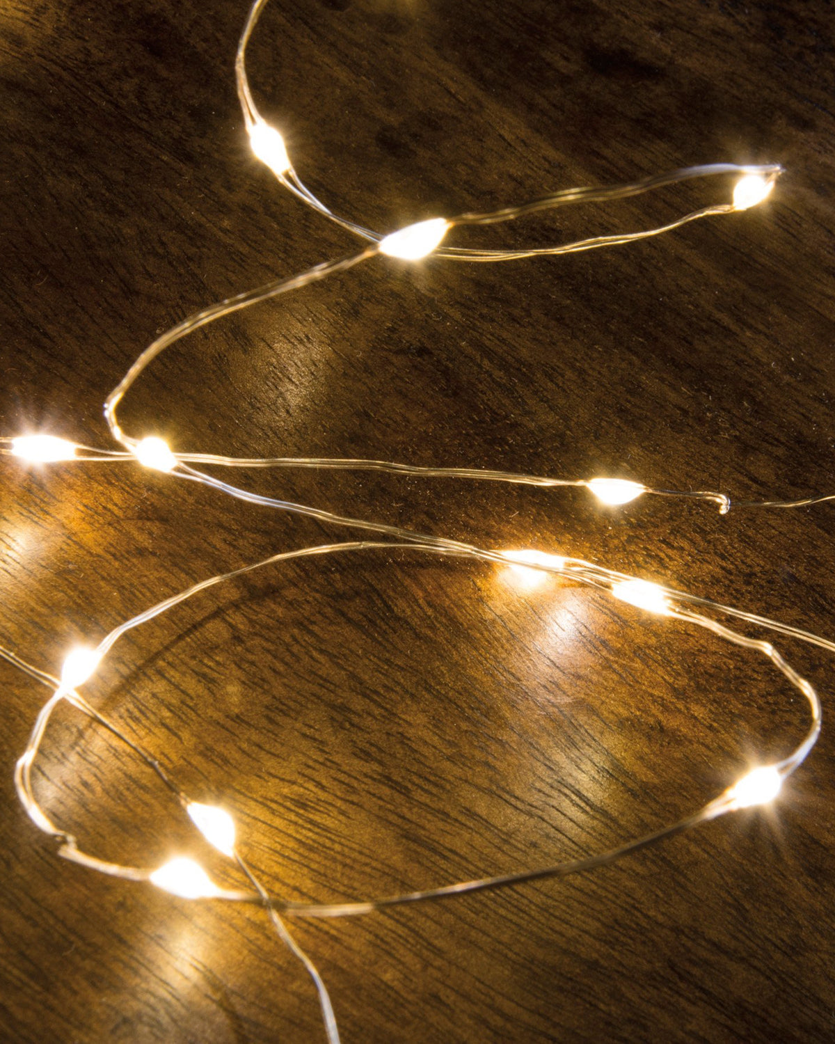 Faire 50 Light Wire String Lights with warm white micro bulbs coiled on a dark wooden surface.