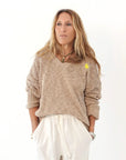 A woman with long, light brown hair wears the Kerri Rosenthal Summerland V Neck Sweater with sleeves rolled up and loose white pants, standing against a white background with her hands in her pockets.