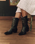 The Great Inc. Southwest Cowboy Boot with gold sunburst design, styled with a white lace dress in a chic setting.