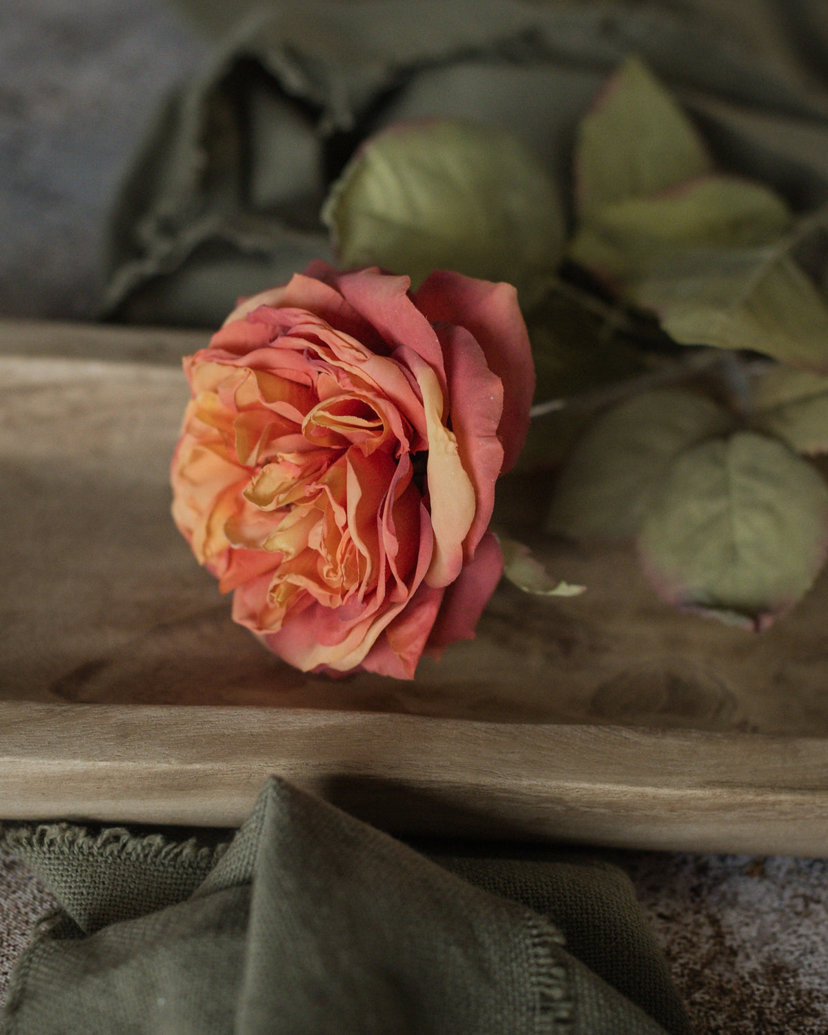 Peach rose with green leaves on olive-green fabric tray, The Faire 19″ Sunset Dried Rose Spray, Bungalow Furniture.