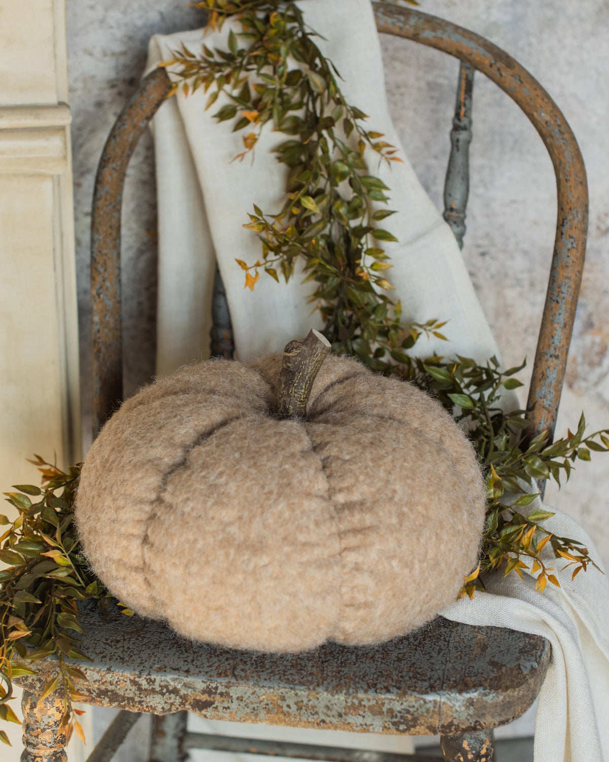 Tan fabric pumpkin, 8.25″, by Faire displayed on a rustic chair with greenery, cozy fall accent.