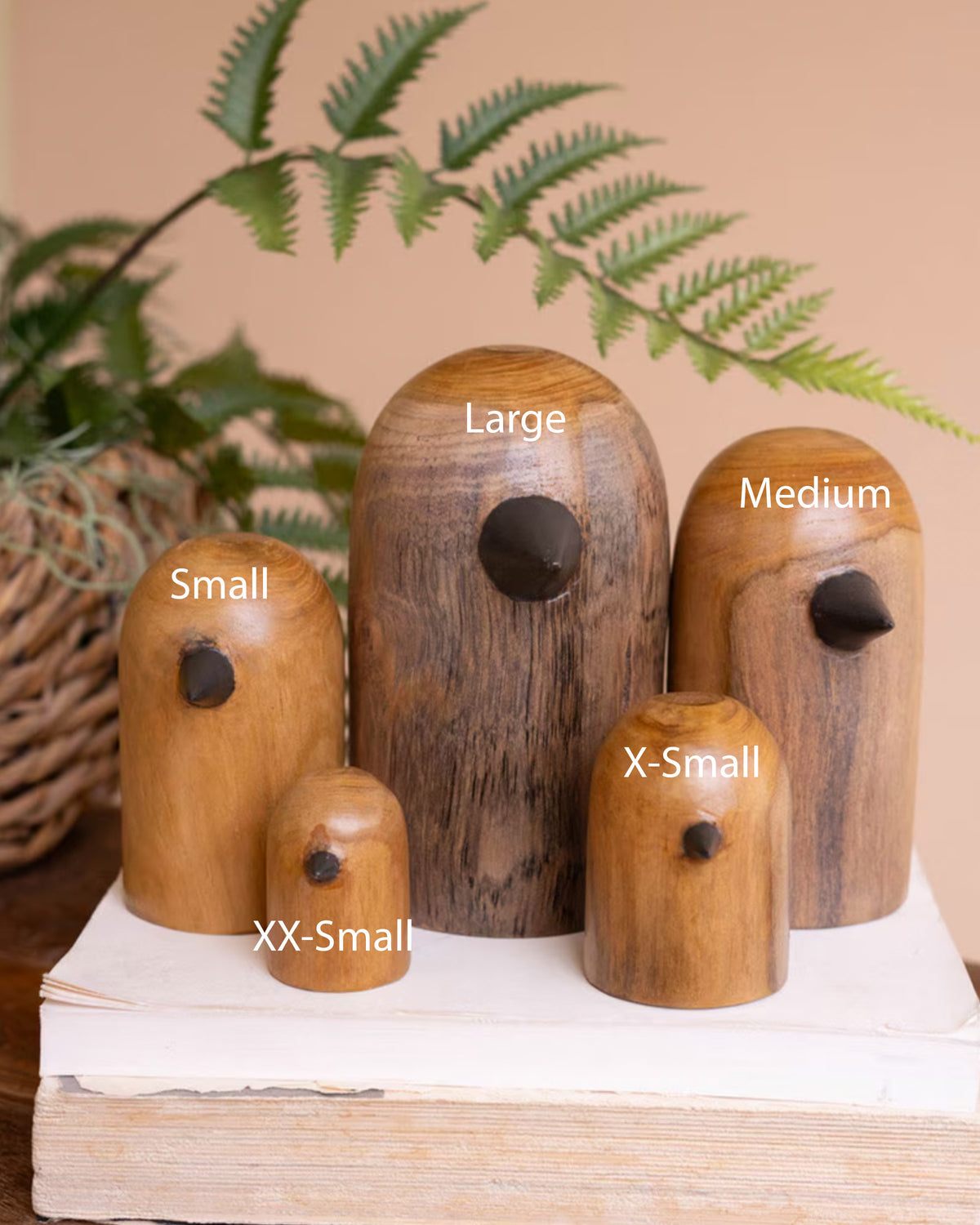 Set of Kalalou teak wood bird sculptures displayed on a book with natural decor in a cozy, organic setting.