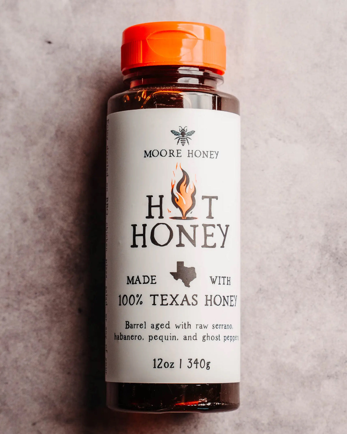 A 12oz (340g) bottle of Faire Texas Hot Honey with an orange cap and white label, made from 100% Texas wildflower honey infused with serrano, habanero, pequin, and ghost peppers for a spicy kick.