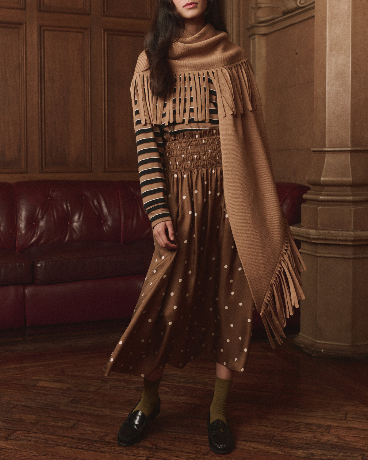The Big Sweater Fringe Scarf by The Great Inc. styled with playful stripes and polka dots in a cozy indoor setting.