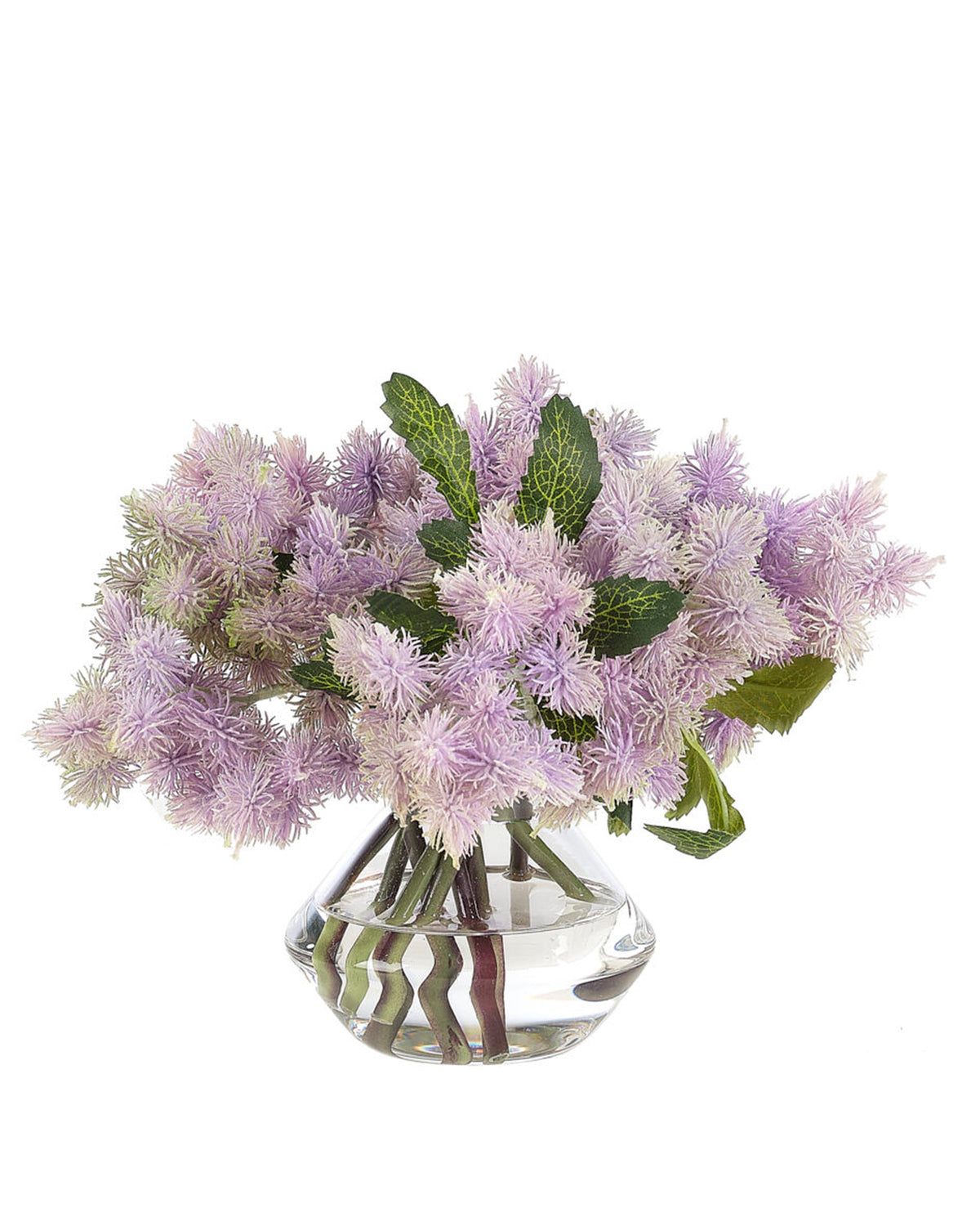 The Thistle Glass Vase by Natural Decorations Inc. features lifelike light purple thistle blooms with feathery textures and green leaves, arranged loosely in a small glass vase against a white background.