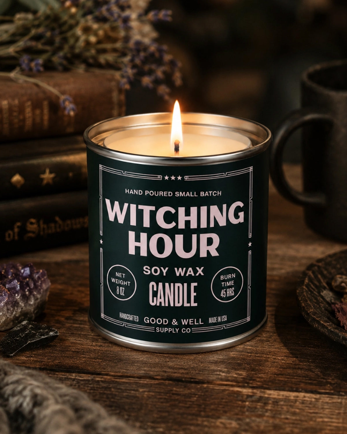 Faire Witching Hour Soy Candle lit beside books and dried florals for a cozy, moody Halloween setting by Bungalow Furniture.