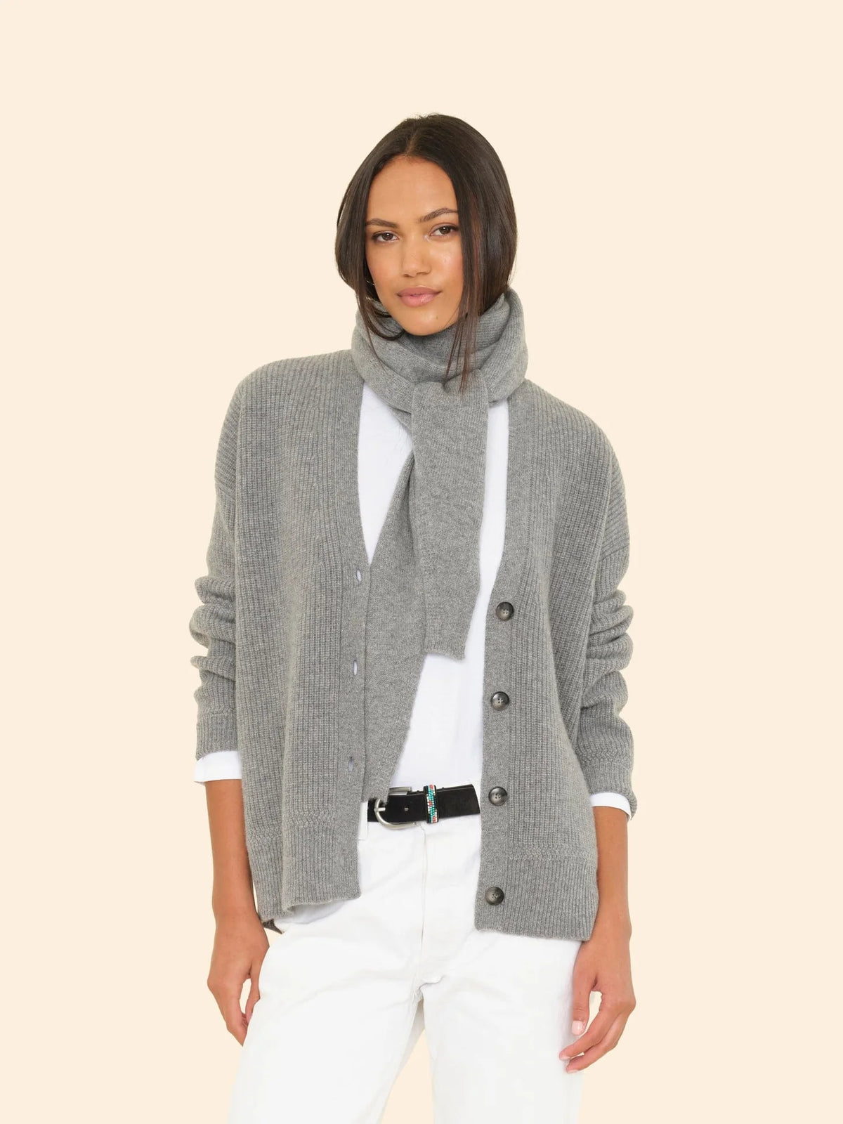 A woman wearing an ultra-soft cardigan and the Le Petit Scarf over a white shirt and pants, posing against a plain light background.